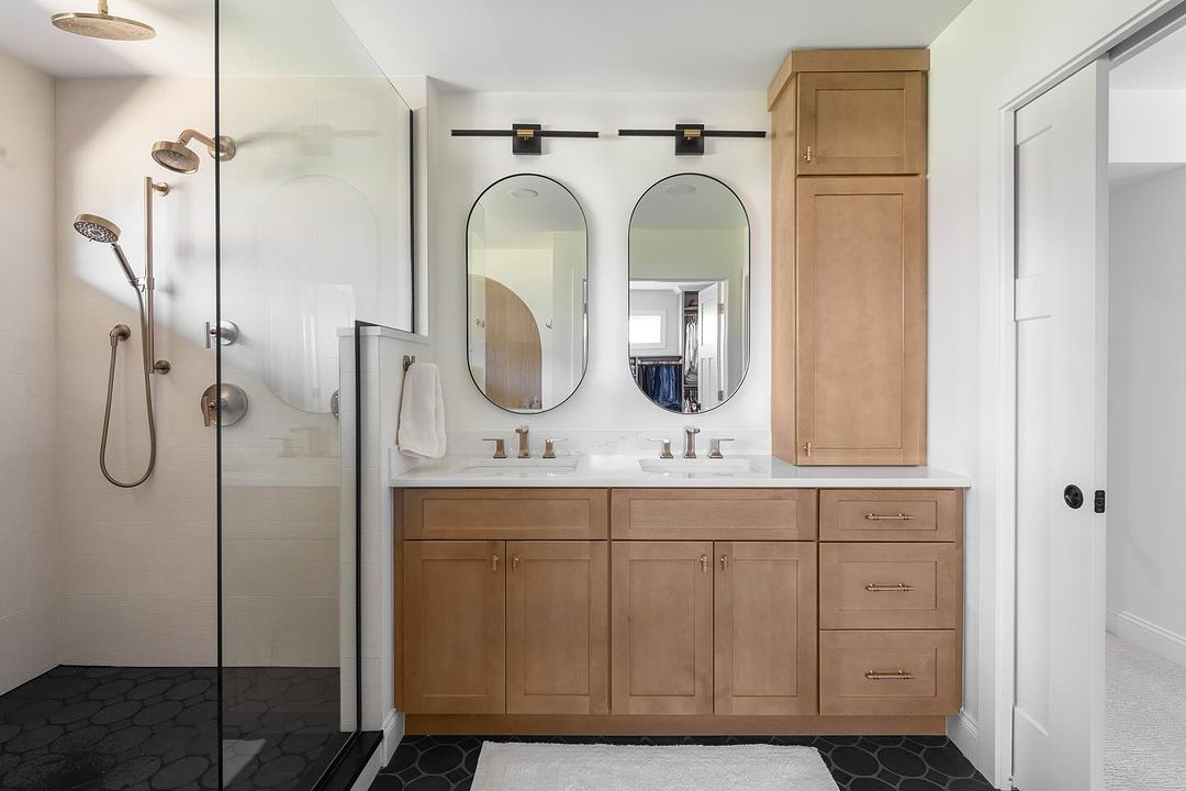 Primary bathroom with a glass walk-in shower, timber double vanity and two oval mirrors